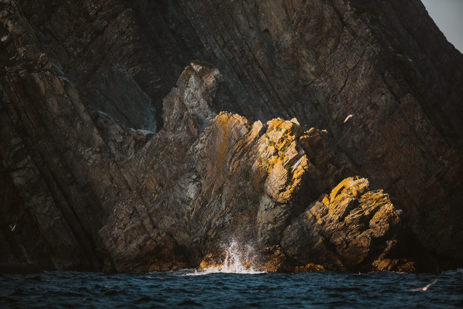 A sunlit wave crashes against the rugged cliffs of the coast in the Discovery Global Geopark along the Bonavista Peninsula