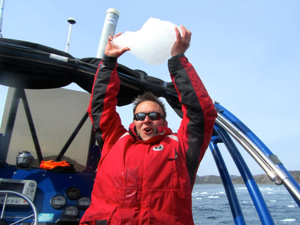 Sea of Whales captain, Kris Prince, excitedly holds up a bergy bit, a small piece of ice broken off from an iceberg, on an iceberg tour along the Bonavista peninsula. 
